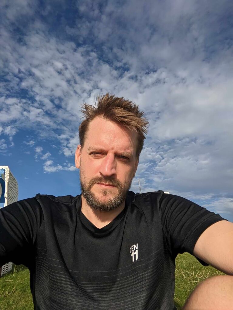 Selfie von Mann vor blauem Himmel mit vereinzelten Wolken.